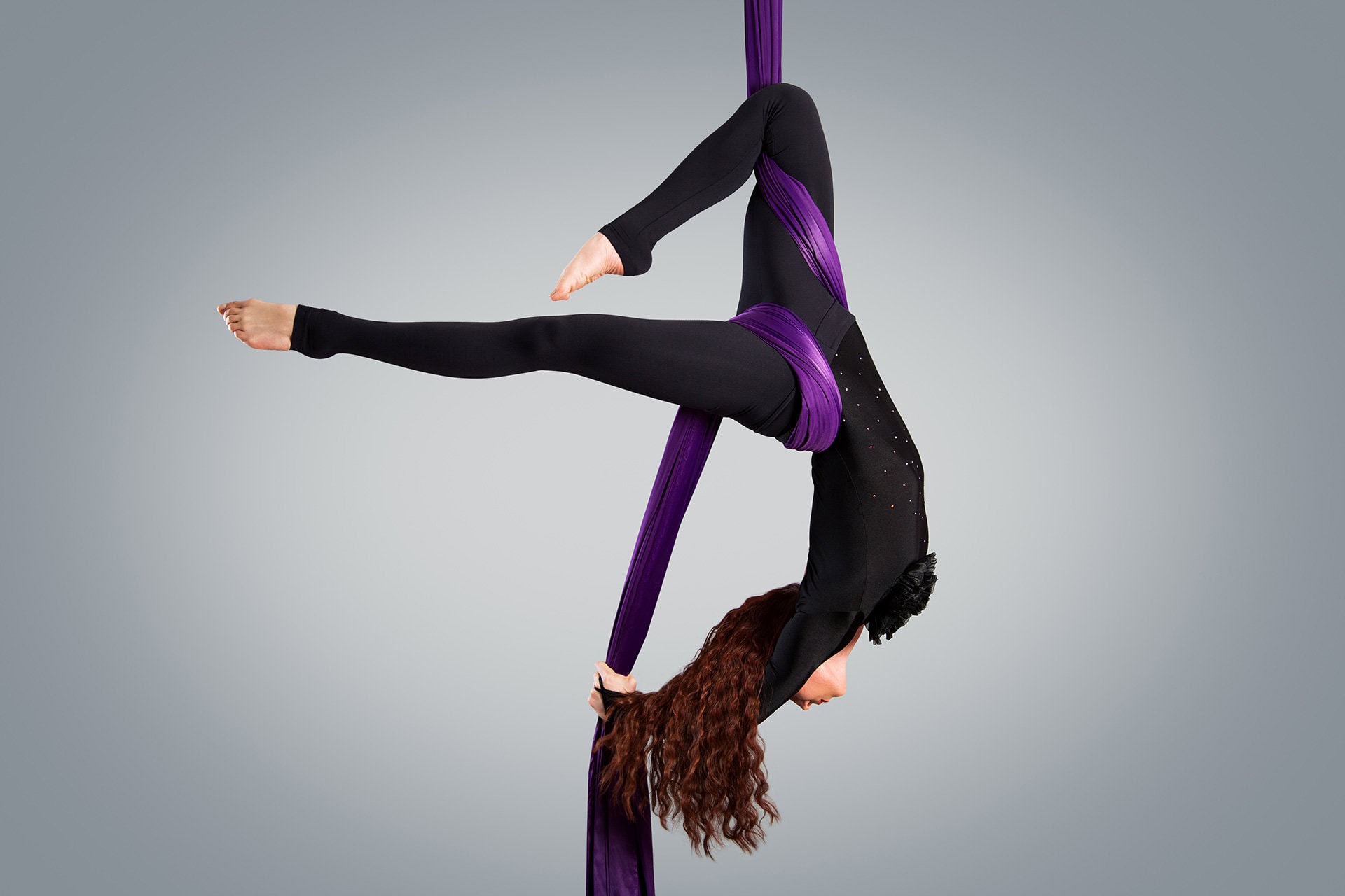Female dancer hanging upside down from aerial silks wearing purple bodysuit
