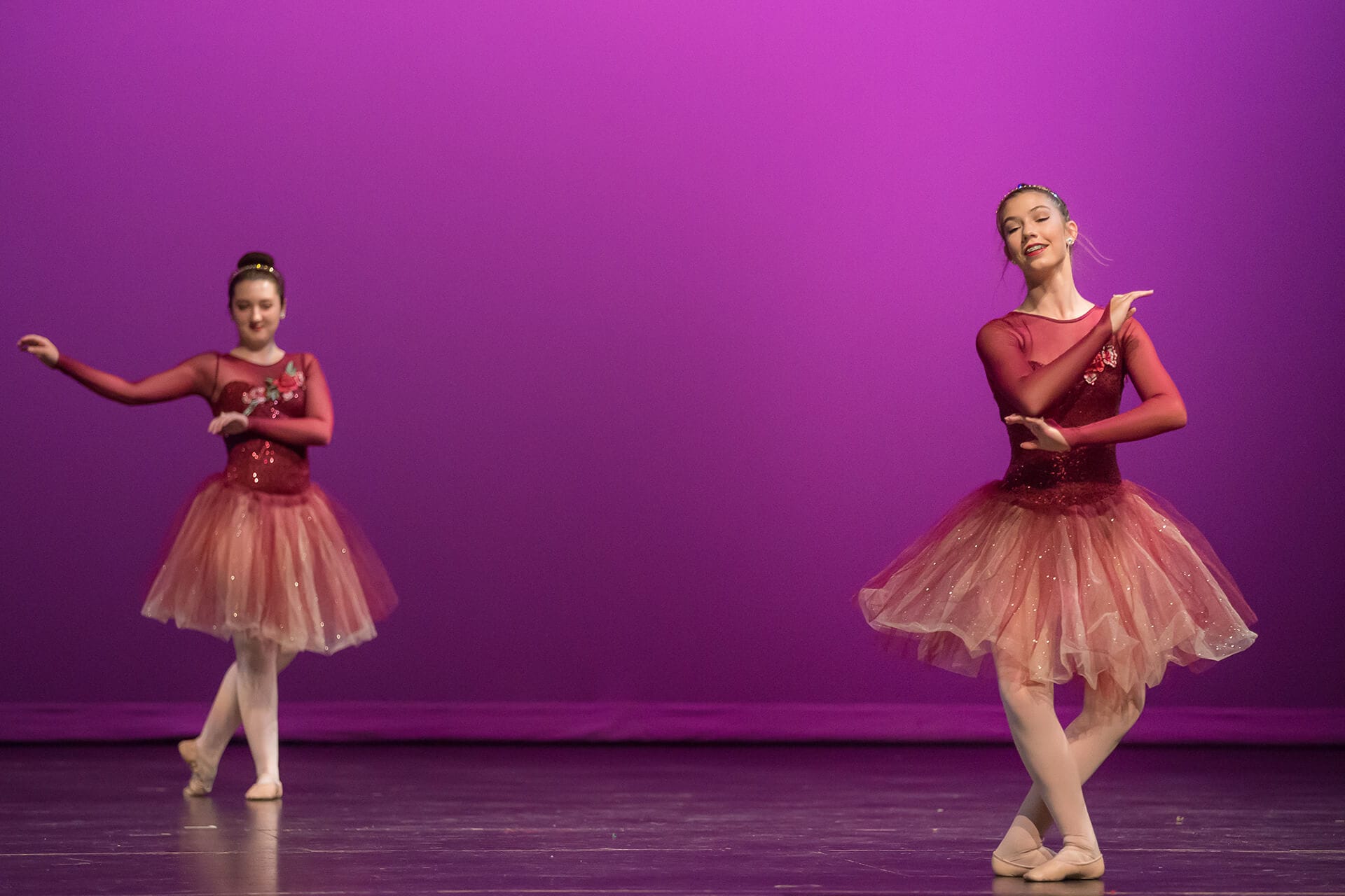 Two female ballet dancers in red costumes against purple stage wall