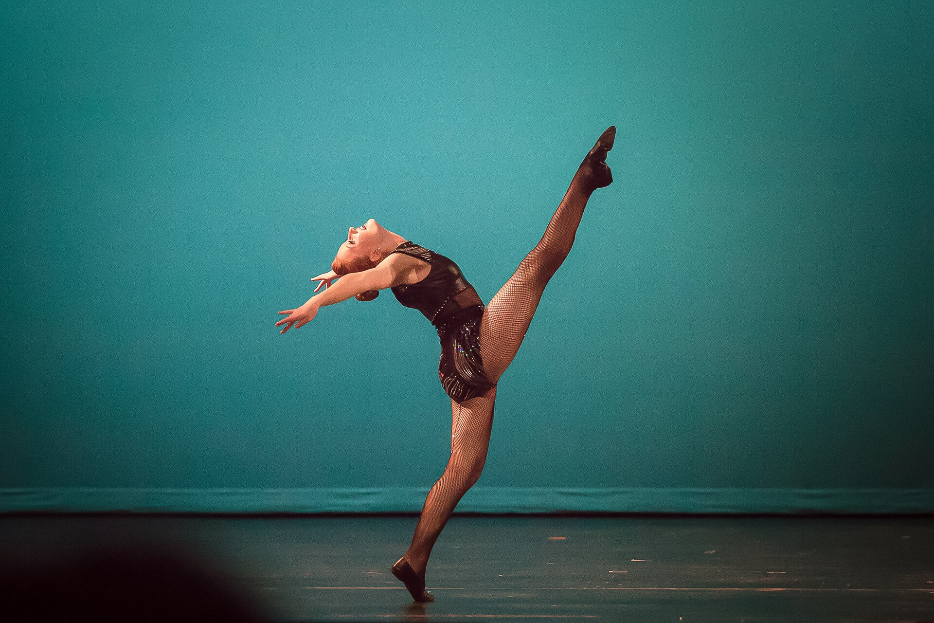 Female dancer with right leg in the air against green backdrop