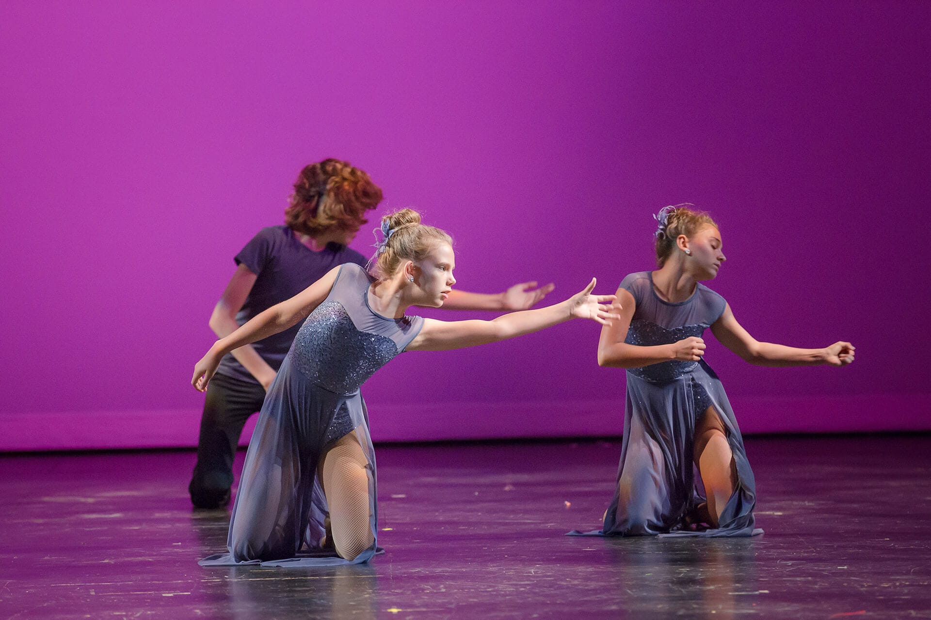 Three contemporary dancers on knees against purple background
