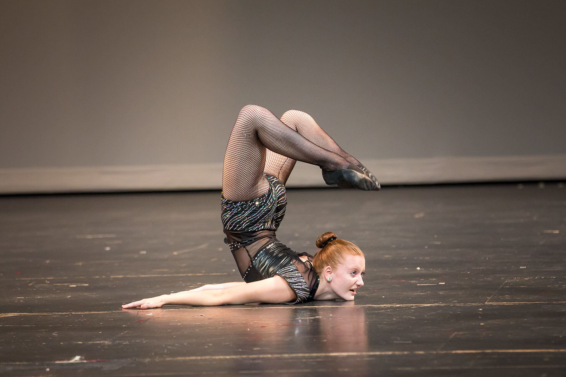 Female dancer with feet above head on beige stage