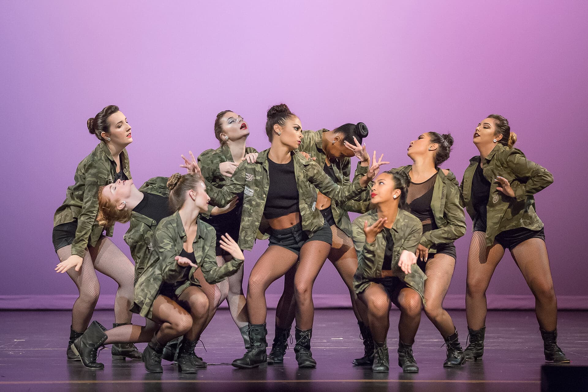 Group of female jazz dancers on stage wearing olive against purple