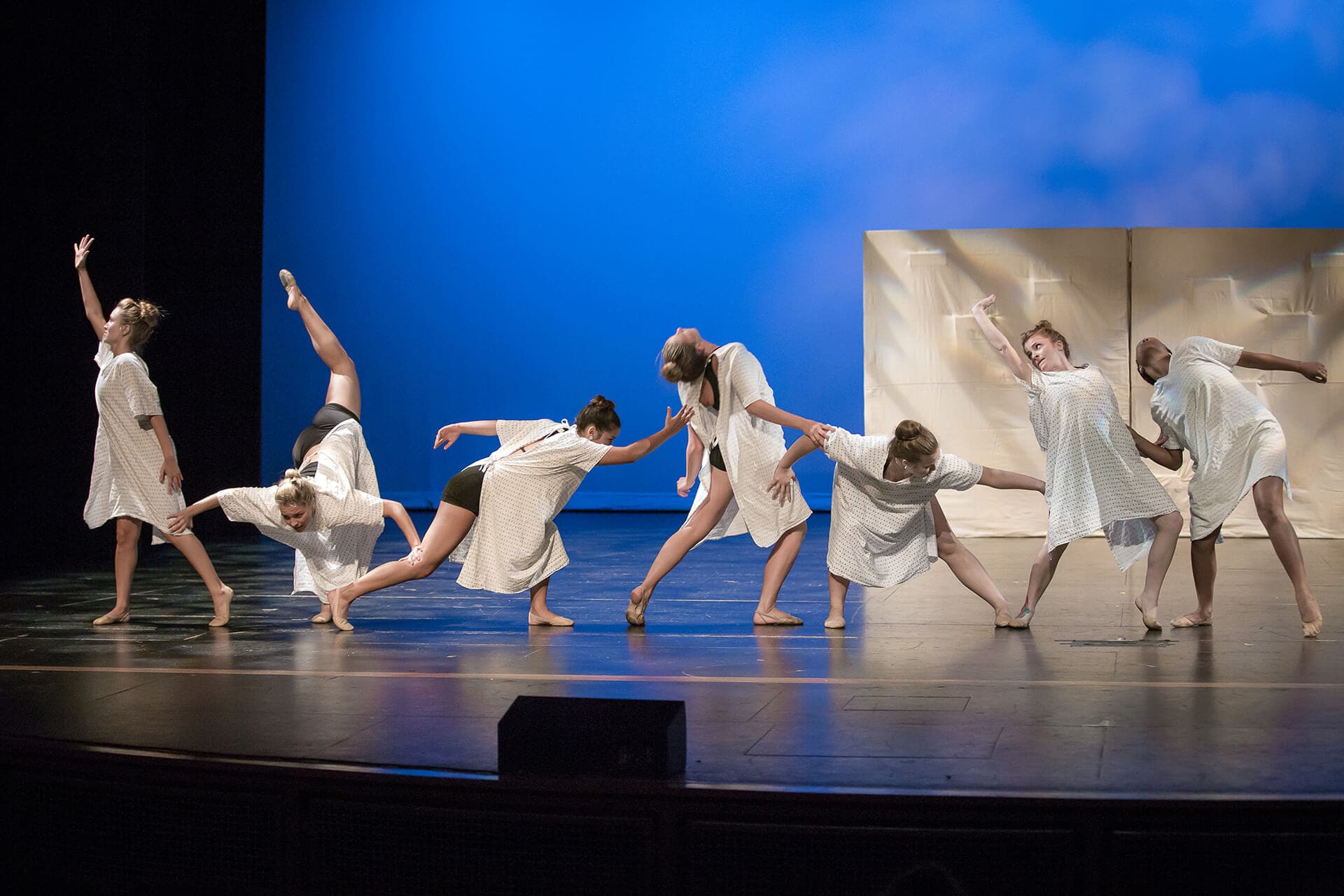 Dancers on stage wearing white against blue background
