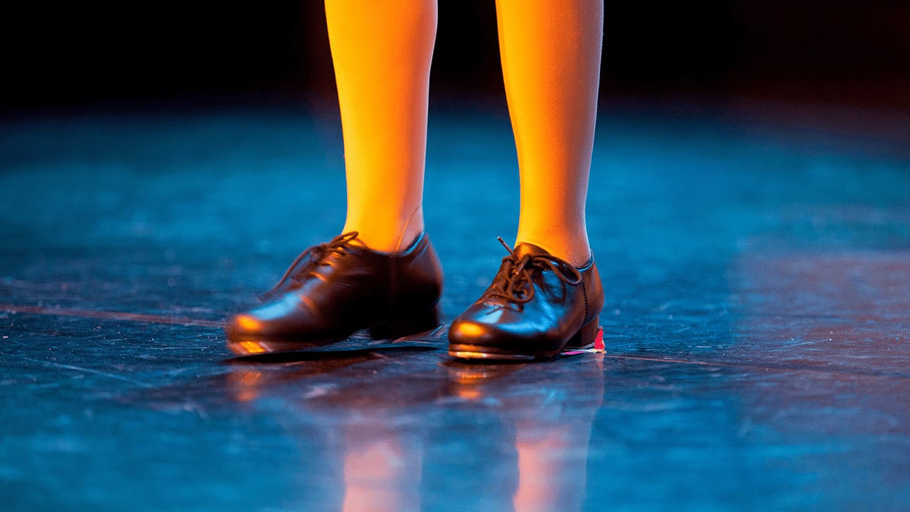 Close of up girl's feet wearing tap shoes on blue stage.