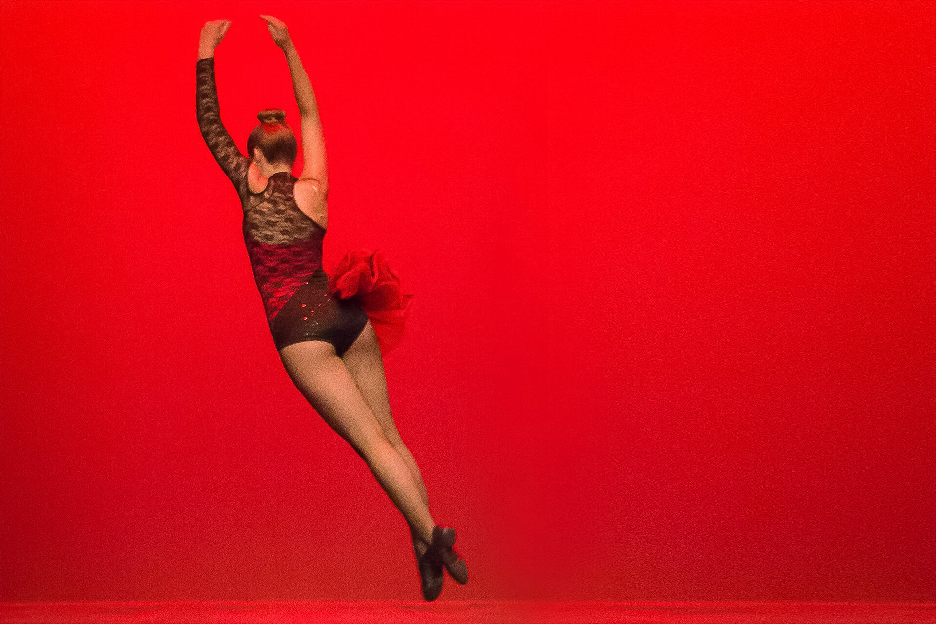 Female dancer in short tutu twirling in air against red background