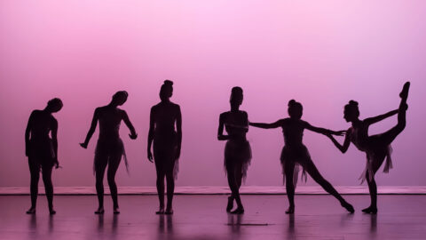 Six ballet dancers in silhouette on stage with pink lighting