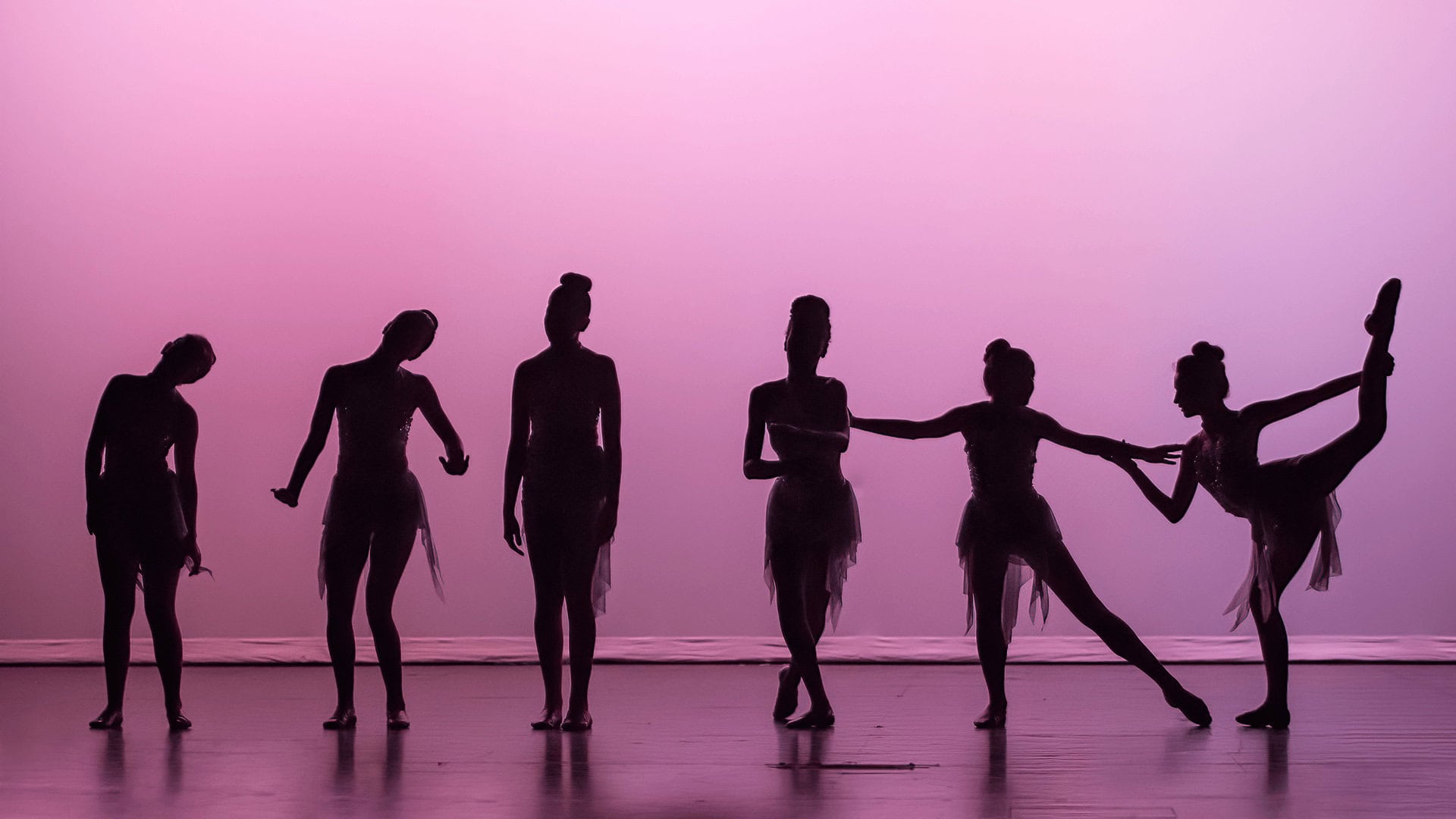 Six ballet dancers in silhouette on stage with pink lighting